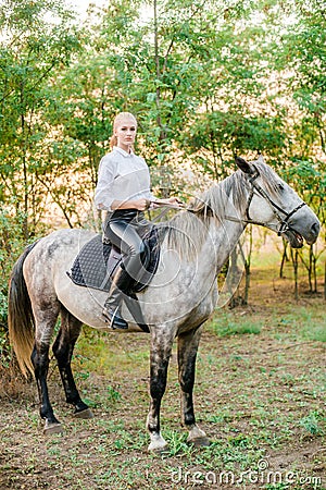 Beautiful young girl with light hair in uniform competition smiling and astride a horse in sunset Stock Photo