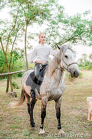 Beautiful young girl with light hair in uniform competition smiling and astride a horse in sunset Stock Photo