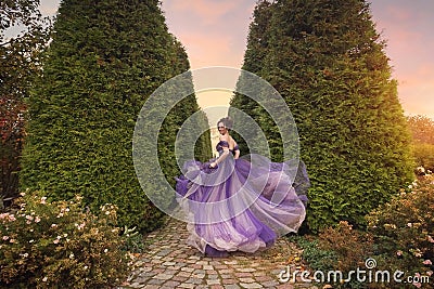 A beautiful young girl in a lilac dress running down the alley of the autumn park. Stock Photo