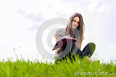 Beautiful young girl with a notebook siting down on lawn Stock Photo