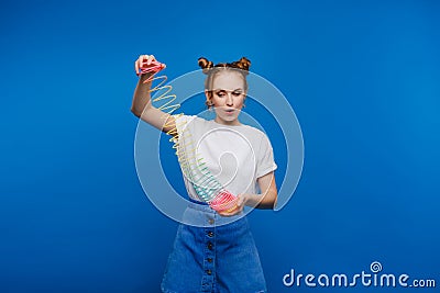 Beautiful young girl playing with a rainbow slinky, a toy of her childhood on a blue background Editorial Stock Photo