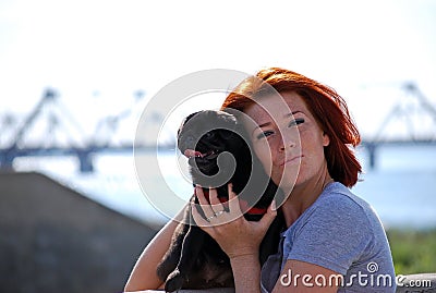 The beautiful young girl with red hair embraces on the street of the pet a black dog of breed a pug. Stock Photo