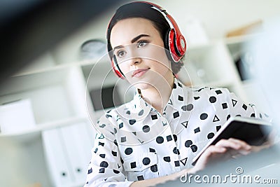 Beautiful young girl sitting in headphones at desk in office. Photo with depth of field, focus on girl. Stock Photo