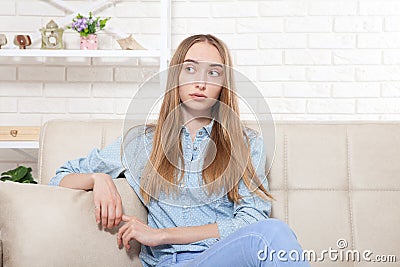 Beautiful young girl sitting on the sofa at home background. Copy space and mock up. Teenager Depression. Sad woman Stock Photo