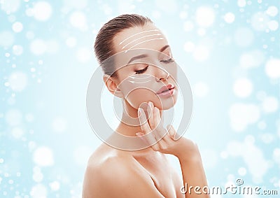 Beautiful young girl touching her face on blue background and snow. Plastic surgery, facelift and rejuvenation concept. Stock Photo