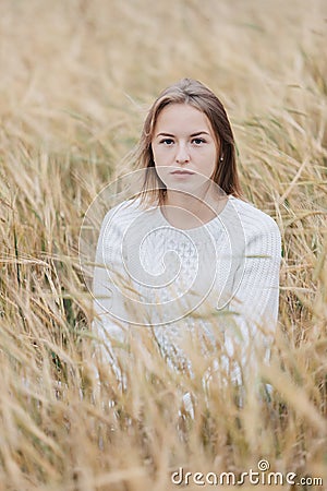 Beautiful young girl in a white sweater sits in a wheat field Stock Photo