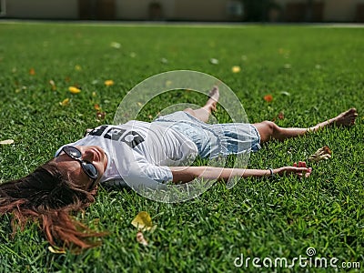 A beautiful young girl in a white T shirt with inscription Break a tree and skirt lies on the grass Stock Photo