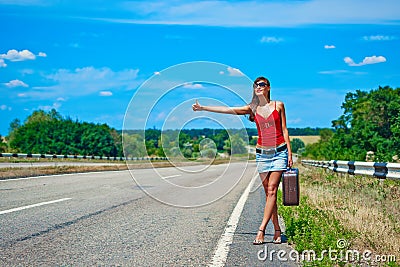 Beautiful young girl or woman in mini with suitcase hitchhiking along a road Stock Photo