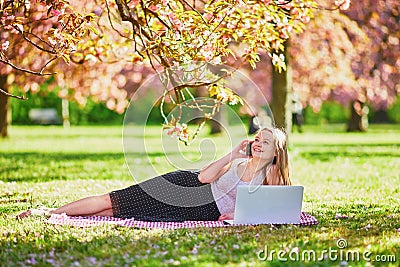 Beautiful young girl working on her laptop in park during cherry blossom season Stock Photo