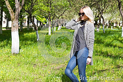 Beautiful young happy blonde girl in coat, jeans and sunglasses walking in the Park on a Sunny day Stock Photo