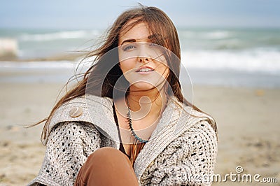 Beautiful young happy woman portrait against seascape, long hair fluttering in the wind, looking at camera, casual autumn fashion Stock Photo