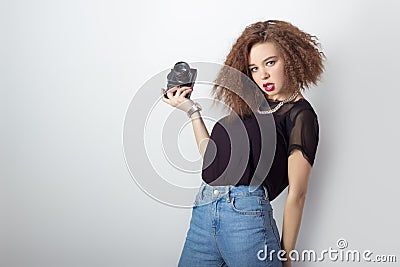 Beautiful young hipster girl holding the camera makes images, photos on the camera, in jeans and a black t-shirt in the Studio Stock Photo