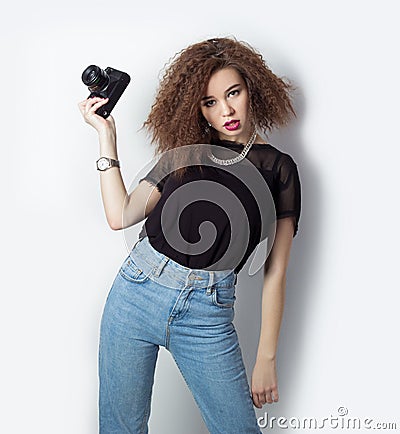 Beautiful young hipster girl holding the camera makes images, photos on the camera, in jeans and a black t-shirt in the Studio Stock Photo