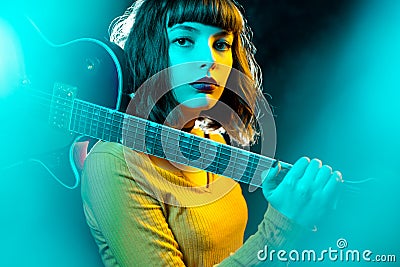 Beautiful young hipster woman with curly hair with red guitar in neon lights. Rock musician is playing electrical guitar Stock Photo