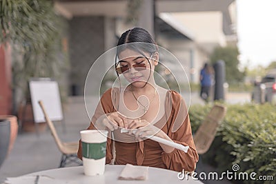 A beautiful young lady wearing a frameless sunglasses attempts to open the straw for her drink Stock Photo