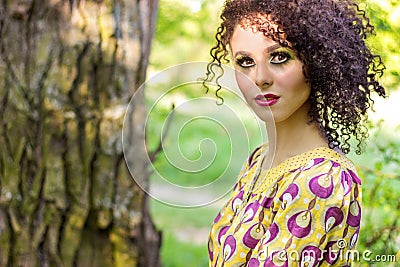 Beautiful young little curly-headed girl with makeup in the summer sun the day sitting on the street Stock Photo