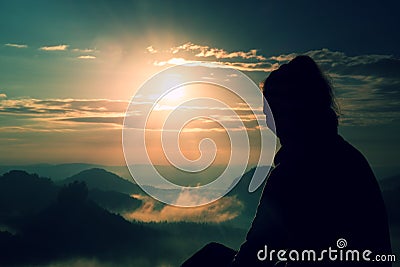 Beautiful young long hair girl tourist enjoy daybreak on the sharp corner of sandstone rock and watch over valley to Sun. Stock Photo