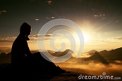 Beautiful young long hair girl tourist enjoy daybreak on the sharp corner of sandstone rock and watch over valley to Sun. Stock Photo