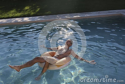 Beautiful young man in swimware floating in a pool at sunset Stock Photo