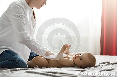 Beautiful young mother in white shirt and jeans putting diaper on cute newborn baby preparing for family dinner with Stock Photo