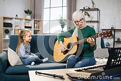 Mother teaching cute little musician girl to play guitar. Stock Photo