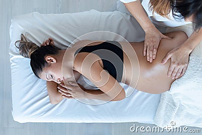 Beautiful young physiotherapist woman massaging tummy on pregnant woman on a stretcher at home Stock Photo