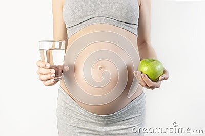 Beautiful young pregnant woman holding green apple and glass of water in her hands on white background. The concept of expectation Stock Photo