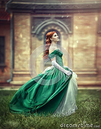 Beautiful, young, red-haired girl in a green medieval dress, climbs the stairs to the castle. Stock Photo