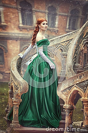 Beautiful, young, red-haired girl in a green medieval dress, climbs the stairs to the castle. Fantastic photosession. Stock Photo