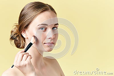Beautiful young redhead woman with freckles contouring her cheekbones using make up brush. Beauty portrait. Stock Photo