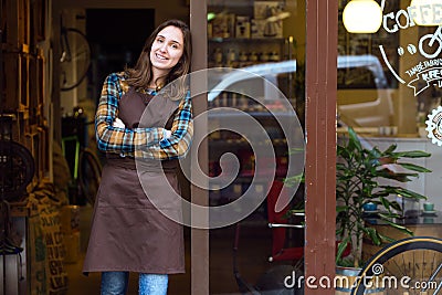 Beautiful young saleswoman looking at camera and leaning against the door frame of an organic store. Stock Photo