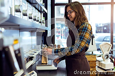 Beautiful young saleswoman weighing coffee beans in a retail store selling coffee. Stock Photo