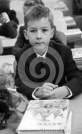 Beautiful young schoolboy sitting at wooden desk in school uniform during lesson Editorial Stock Photo