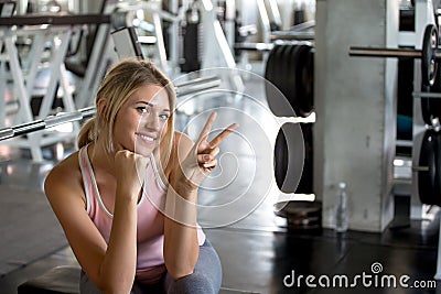 Beautiful young sport woman taking a break from exercise showing v-sign in fitness gym .girl in sportswear workout rest Stock Photo