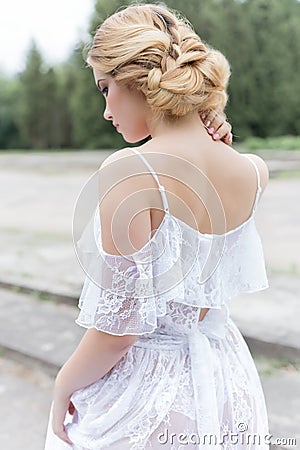 Beautiful young sweet blonde girl with wedding bouquet in the hands of the boudoir in a white dress with evening hairstyle walks Stock Photo