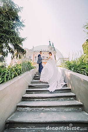 Beautiful young wedding couple on stairs in park. Romantic antique palace at background Stock Photo