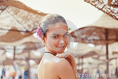 Beautiful young woman in bikini smear protective cream on the skin on the beach under the sun. Stock Photo