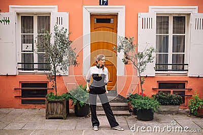 A beautiful young woman in a black fashionable jumpsuit stands on a Parisian street with colorful bright houses Editorial Stock Photo