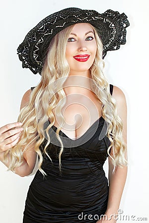 Beautiful young woman blonde in black dress and hat with decollete. Stock Photo