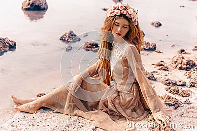 Beautiful young woman in boho dress and wreath on the beach at sunset Stock Photo