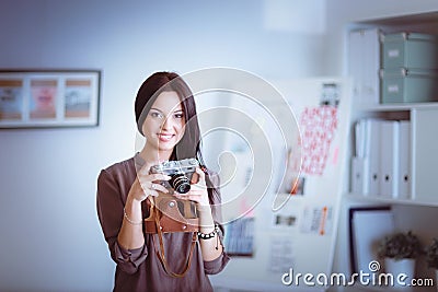 Beautiful young woman with camera standing near desl in office Stock Photo