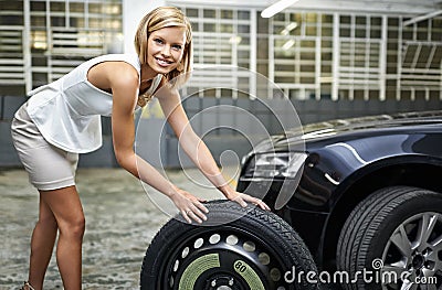 No need for men. A beautiful young woman changing her cars tyre in a parkade. Stock Photo