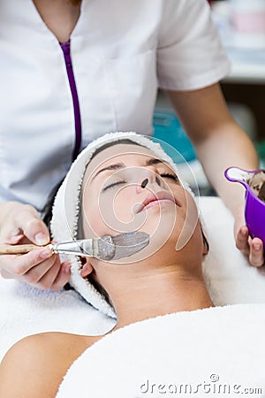 Beautiful young woman with clay facial mask in beauty spa. Detox Stock Photo