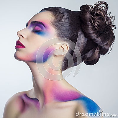 Beautiful young woman with creative colored makeup and curly collected hairstyle and painted colored body. Stock Photo