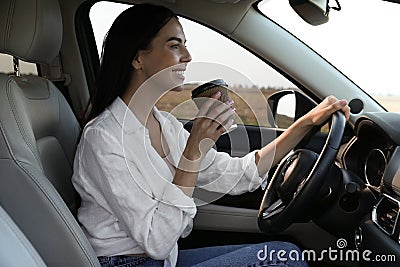 Beautiful young woman with cup of coffee driving her modern car Stock Photo