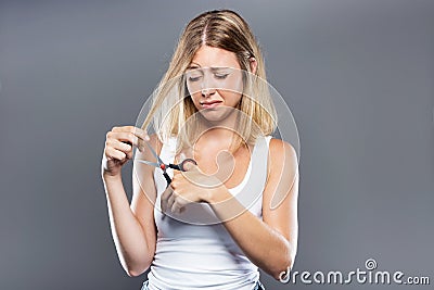 Beautiful young woman cutting her hair over gray background. Stock Photo