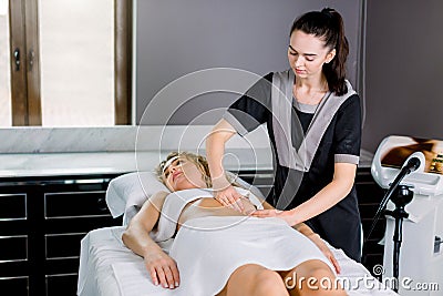 Beautiful young woman doctor massage therapist in a cosmetology room doing an abdomen massage to young blond woman Stock Photo