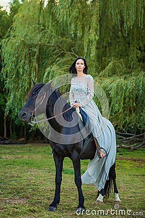 Beautiful young woman in beautiful dress on black horse in nature Stock Photo