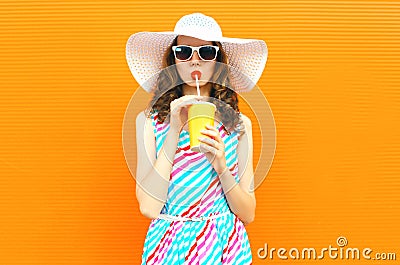 Beautiful young woman drinking juice in summer straw hat, colorful striped dress on orange wall Stock Photo