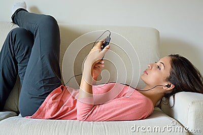 Beautiful young woman with earphones relaxing on the sofa, she is listening to music using a smart phone, chill out and leisure Stock Photo